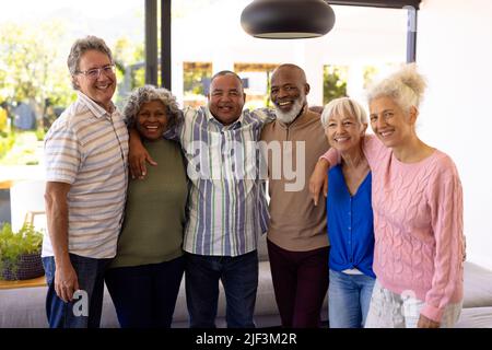 Portrait d'amis âgés gais et multiraciaux avec les bras autour debout dans la maison de soins infirmiers Banque D'Images