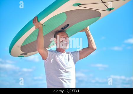 Homme portant une planche de surf sur la tête contre le ciel Banque D'Images