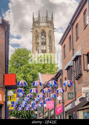 Parasols Union Jack suspendus au-dessus de Coppergate Walk avec la tour octogonale de l'église de tous les Saints pavé au loin. York. Banque D'Images