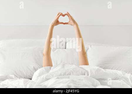 mains de la femme allongé dans le lit et faisant la forme du coeur Banque D'Images