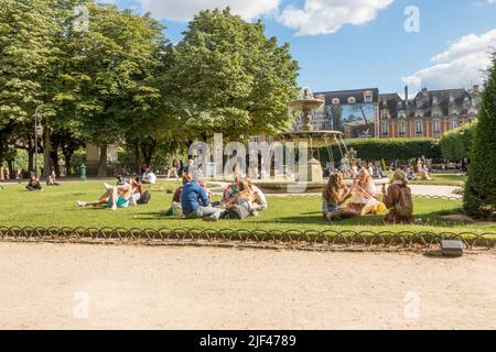 Place des vosges, Paris. Les gens se détendent par une chaude journée près de la fontaine de la plus ancienne place de Paris, en France. Banque D'Images