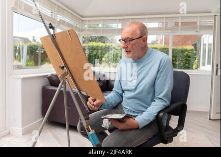 Portrait environnemental d'un homme âgé peint avec des aquarelles dans son studio à la maison Banque D'Images