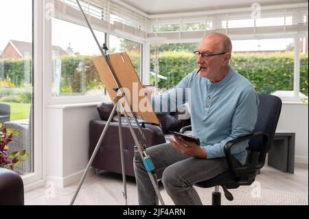 Portrait environnemental d'un homme âgé peint avec des aquarelles dans son studio à la maison Banque D'Images