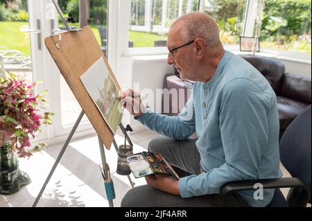 Portrait environnemental d'un homme âgé peint avec des aquarelles dans son studio à la maison Banque D'Images