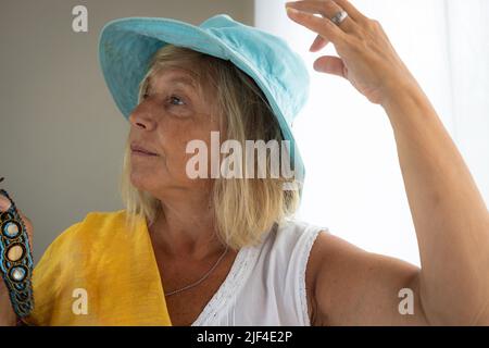 Femme de race blanche d'âge moyen par une fenêtre. Femme dans sa maison avec une robe décontractée. Banque D'Images