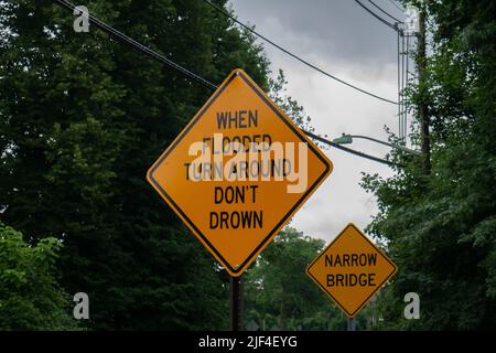 Un gros plan de panneaux orange avec du texte dans le parc. Lors d'un virage inondé, ne pas noyer, pont étroit. Banque D'Images