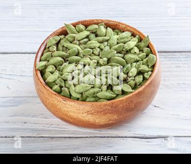 Gousse de cardamome dans un bol en bois sur fond blanc en bois Banque D'Images