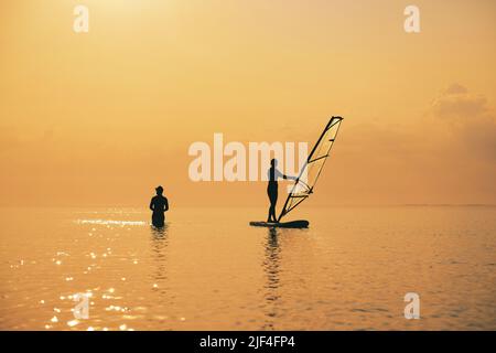 Coucher de soleil sur la mer avec silhouette de fille avec une selle sur un panneau SUP Banque D'Images