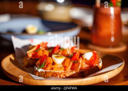 Gros plan sur une entrée de pain grillé au saumon ou un hors-d'œuvre avec des œufs et des tomates sur une table en bois au restaurant. Tranche de pain avec saumon fumé salé et boisson Banque D'Images