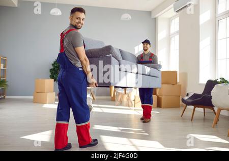 Deux jeunes travailleurs heureux de la compagnie de déménagement et du service de livraison portant un lourd canapé Banque D'Images