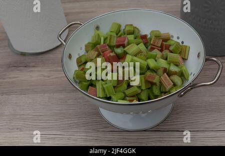 Morceaux de rhubarbe rouge et vert hachés dans une passoire en émail blanc sur une surface en bois pâle Banque D'Images