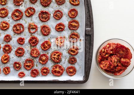 Tomates fraîchement séchées aux herbes sur la plaque de cuisson et dans un bol en verre Banque D'Images