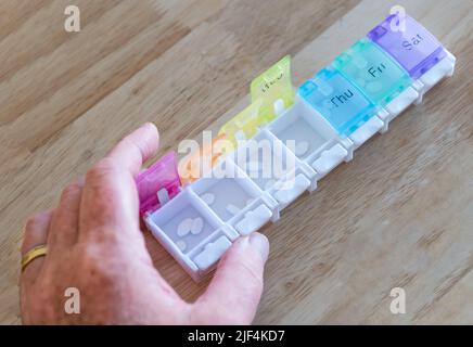 Un homme organisant des comprimés ou des pilules hebdomadaires de médicaments dans un organisateur de pilules avec les jours de la semaine marqués, Royaume-Uni Banque D'Images