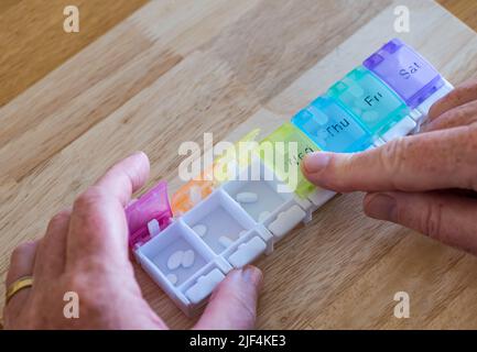Un homme organisant des comprimés ou des pilules hebdomadaires de médicaments dans un organisateur de pilules avec les jours de la semaine marqués, Royaume-Uni Banque D'Images