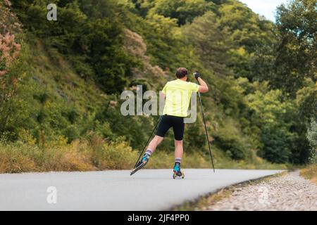 Entraînement de biathlon. Entraînement d'homme sportif sur le roller ski sur la route de campagne, vue arrière. Concept de compétition et d'activité d'été. Banque D'Images