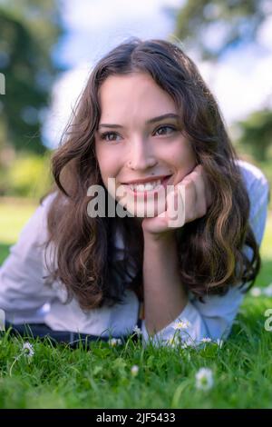 Portrait d'une jeune femme en décubitus ventral sur l'herbe dans un parc Banque D'Images