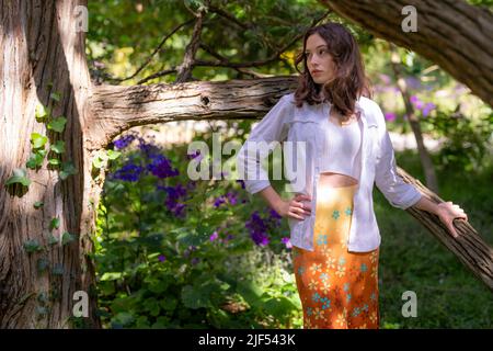 Jeune femme debout dans un jardin entouré d'arbres et de fleurs | Jupe à fleurs Banque D'Images