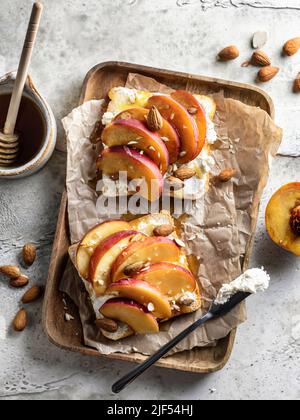 Toast avec fromage à la crème, pêche fraîche juteuse, amande et miel sur un plateau en bois. Apéritif ou en-cas d'été sains, vue de dessus Banque D'Images