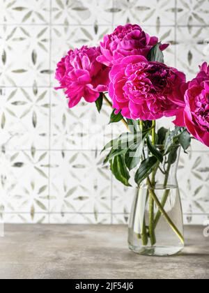 Magnifique bouquet de pivoines roses dans un vase sur une table sur fond de carreaux. Espace pour le texte. Orientation verticale Banque D'Images