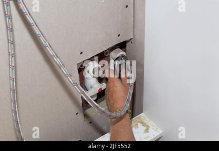 Installation du robinet de cuisine. La plombier fixe le raccord de tuyau flexible à l'aide d'une clé réglable. Réparation à la maison. Banque D'Images