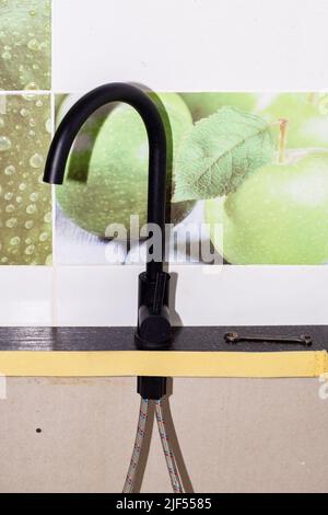 Installation du robinet de cuisine. Un grand robinet noir boulonné au comptoir de cuisine. Réparation à la maison. Banque D'Images