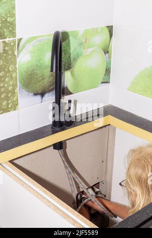 Installation du robinet de cuisine. La plombier fixe le raccord de tuyau flexible à l'aide d'une clé réglable. Réparation à la maison. Banque D'Images