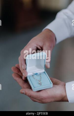 Croix de l'enfant dans les mains des hommes dans un boîtier bleu. Mise au point sélective. Banque D'Images