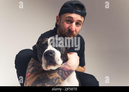 Barbu homme caucasien hugs amstaff chien studio tourné fond gris isolé copie espace . Photo de haute qualité Banque D'Images