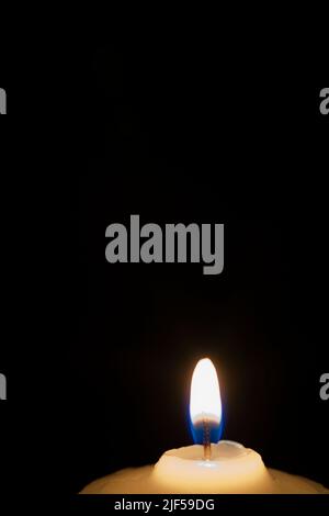 Gros plan d'une bougie de cire blanche avec une flamme bleue sur fond noir. Banque D'Images