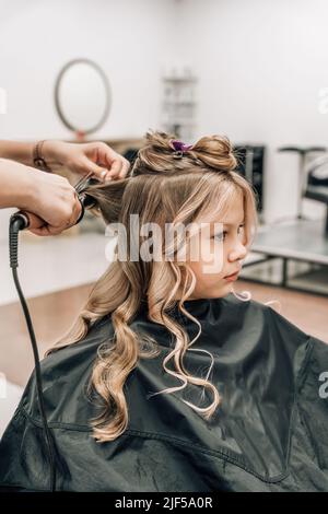 Coiffure de petite fille. Mains utilisant des fers à friser. Photo de haute qualité Banque D'Images