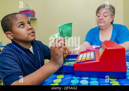 Un tuteur bénévole aide un étudiant à faire des changements avec une caisse de jouets dans un centre de tutorat après l'école, le 28 février 2013, à Columbus, Mississippi. Banque D'Images