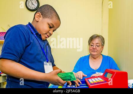 Un tuteur bénévole aide un étudiant à faire des changements avec une caisse de jouets dans un centre de tutorat après l'école, le 28 février 2013, à Columbus, Mississippi. Banque D'Images