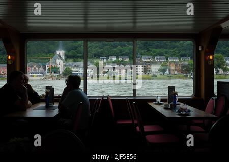 Ferry de Bingen-Rudesheimer vue de Sankt Goarshausen à travers les fenêtres du restaurant pendant qu'il navigue sur le Rhin. Passagers sur une table en silhouette. Banque D'Images