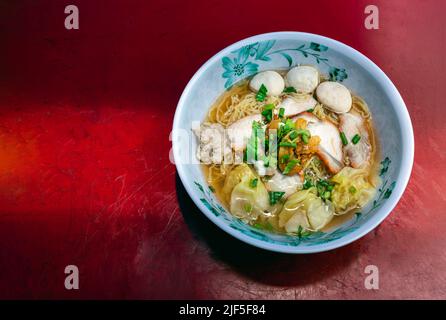 Soupe traditionnelle aux nouilles aux œufs avec boule de poisson, porc barbecue rouge, Wontons, porc haché saupoudrer d'oignon de printemps dans un bol blanc sur une table en fer rouge. Asie Banque D'Images