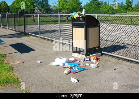 Poubelle débordant d'ordures près d'un terrain de sport dans un parc local. Banque D'Images