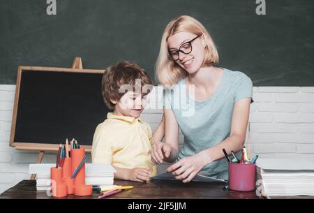 Mère enseignant son fils en classe à l'école. Drôle petit enfant et jeune femme enseignant ayant l'amusement sur fond de tableau noir. Les enfants de l'école. Banque D'Images