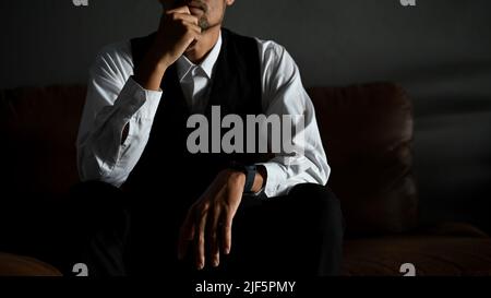 Homme d'affaires asiatique professionnel et réussi ou directeur général masculin dans un costume formel se trouve sur un canapé en cuir dans une posture pensive d'expression de pensée Banque D'Images