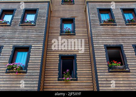 Une photographie d'une façade de bâtiment symétrique avec des garnitures en bois et de nombreuses fenêtres. De beaux géraniums rouges en pots poussent sur les rebords de la fenêtre. Banque D'Images