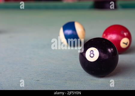 Une vieille boule de billard noire avec le numéro 8 (huit) repose sur le tissu délavé de la table de billard. Banque D'Images