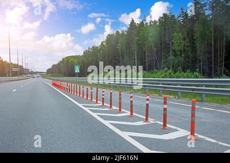 Autoroute à grande vitesse au milieu de la forêt et enregistrement sur la droite, séparés par des marquages et des barres orange sûres Banque D'Images