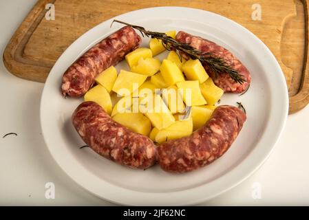 Reliez les saucisses aux pommes de terre fraîches sur une planche à découper en bois isolée sur du blanc avec un espace de copie. Banque D'Images