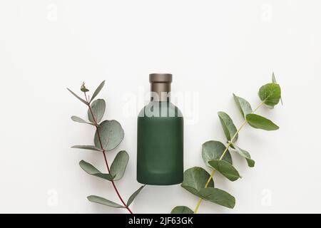 Bouteille de parfum avec branches d'eucalyptus vertes isolées sur fond blanc. Concept de beauté, maquette, vue de dessus Banque D'Images