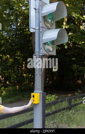 une main féminine appuie sur le bouton pour allumer le feu de circulation au croisement. Photo de haute qualité Banque D'Images