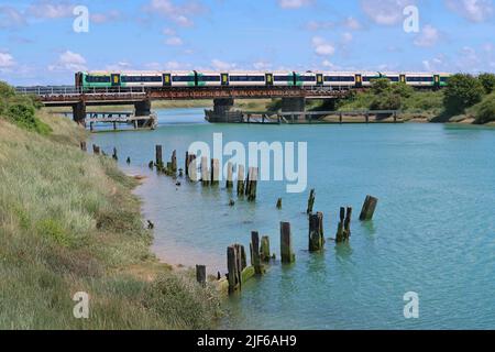 Un train de voyageurs du sud traverse la rivière Arun à Ford, près de Littlehampton, dans le West Sussex. Affiche les restes de la jetée en bois au premier plan. Banque D'Images