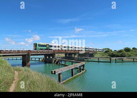 Un train de voyageurs du sud traverse la rivière Arun à Ford, près de Littlehampton, dans le West Sussex. Affiche les restes de la jetée en bois au premier plan. Banque D'Images