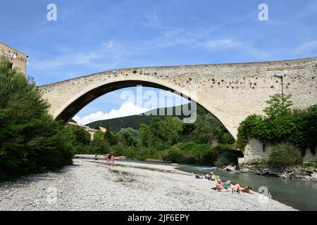 Les touristes se bronzent et se détendent le long de la rivière Aigues sous le pont médiéval Single Span, connu sous le nom de pont romain, Nyons Drôme Provence France Banque D'Images