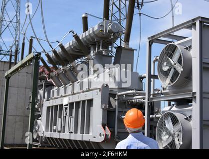 22 juin 2022, Saxe-Anhalt, Bad Lauchstädt : un employé se trouve devant un transformateur 380 000 V à la sous-station Bad Lauchstädt. La sous-station est l'un des plus de 70 centres d'électricité exploités par l'exploitant du réseau de transport 50hertz dans l'est de l'Allemagne et doit être élargie dans le cadre de la transition énergétique. Deux STATCO sont construits ici pour collecter l'électricité des énergies renouvelables, la transformer en tension plus élevée et la transporter vers d'autres régions par des lignes à très haute tension. Les installations de haute technologie sont destinées à maintenir la tension dans le réseau électrique à un niveau constant Banque D'Images