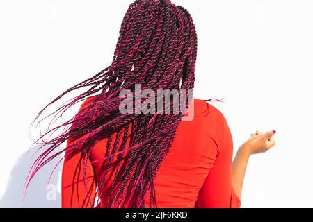 Vue arrière de la femme afro-américaine anonyme en robe rouge tendance et tresses sur fond blanc Banque D'Images