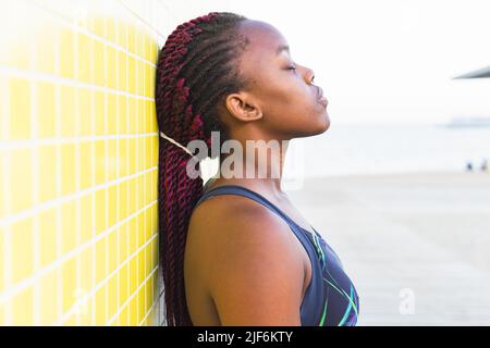 Jeune femme noire en robe africaine authentique et vivante avec des petits pains à cheveux et un maquillage traditionnel se repliant les mains sur le ventre et regardant l'appareil photo tout en étant debout Banque D'Images