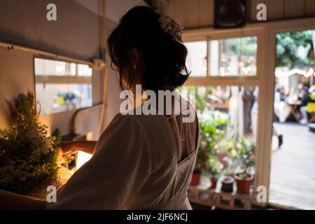 Vue arrière de la jeune mariée en robe blanche regardant le bouquet de fleurs et préparant pour la célébration de mariage dans la chambre confortable Banque D'Images